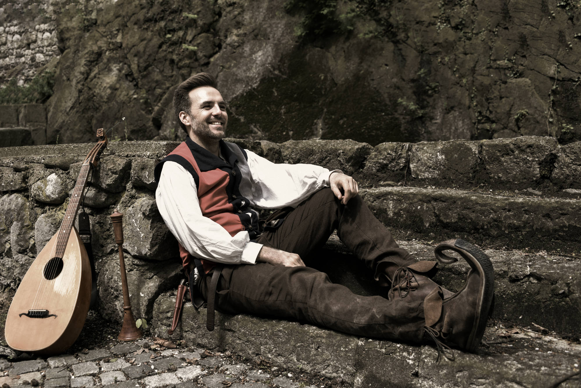 Barde Barlhow mit Instrument vor einer Steinmauer