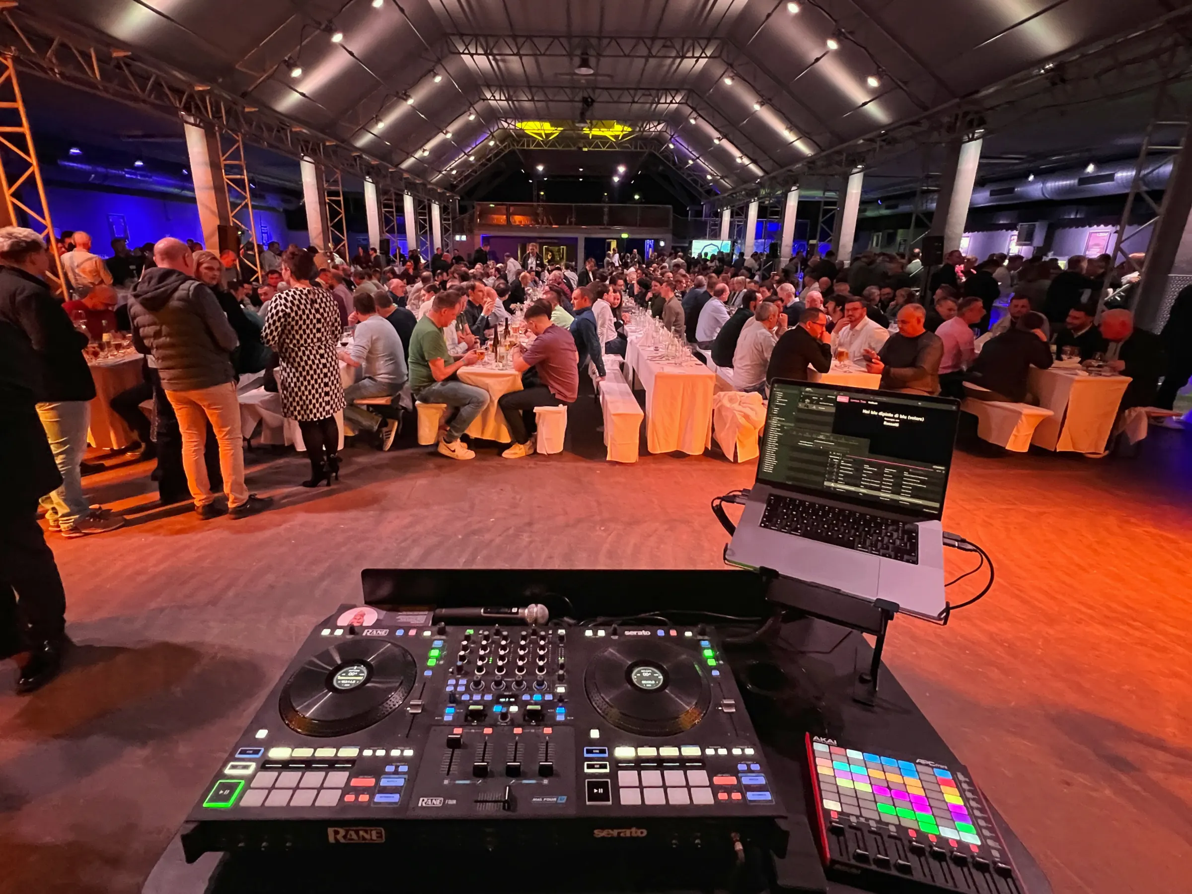 DJ-Pult mit Blick auf eine volle Veranstaltung und viele Gäste